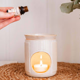 Person holding a bottle of essential oil above a lit candle in a ceramic holder with eucalyptus leaves in the background.