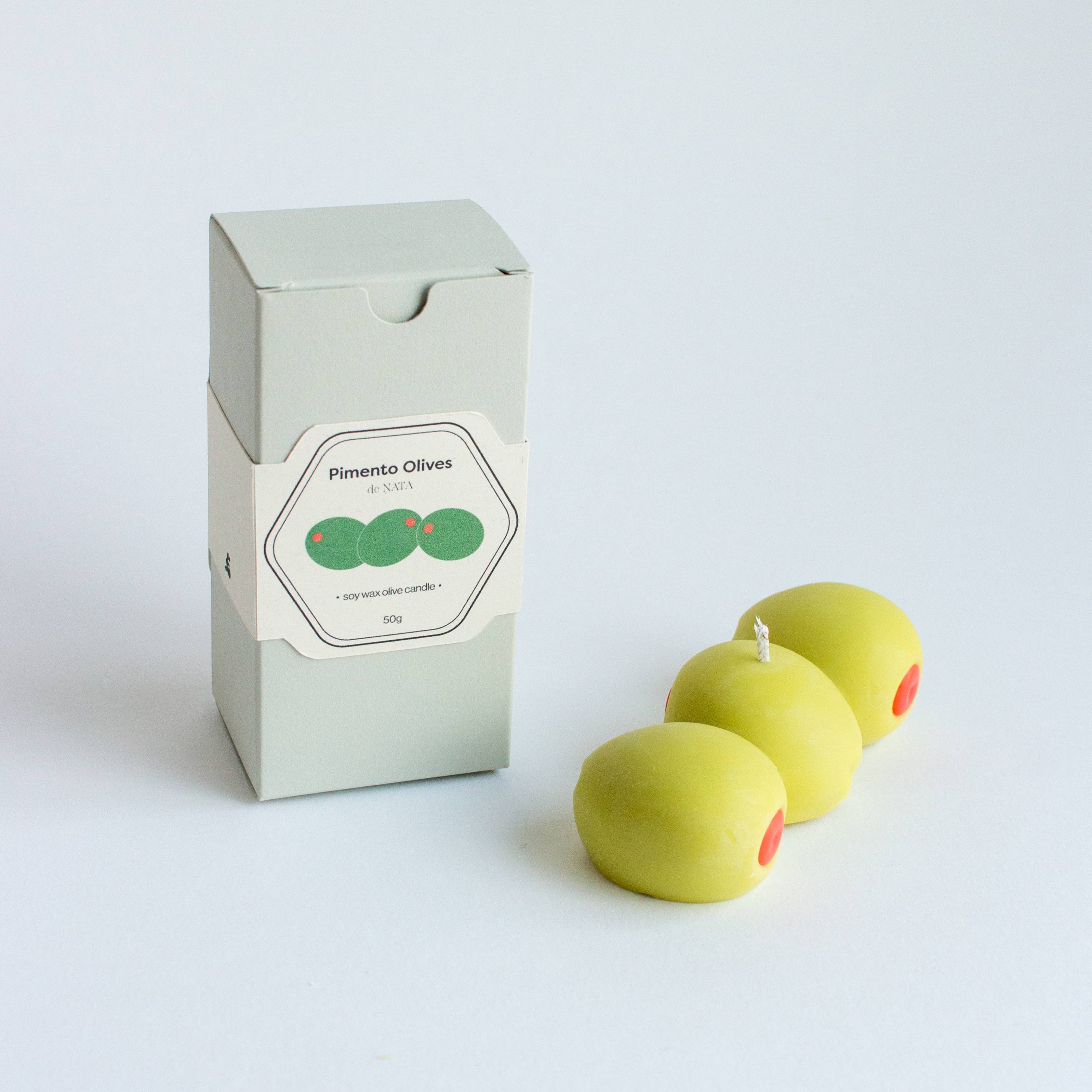 Three green olives with red stems next to a box labeled 'Pimento Olives' on a white background