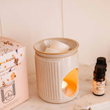Ceramic diffuser with a lit candle, packaging, and essential oil bottle on a shelf.