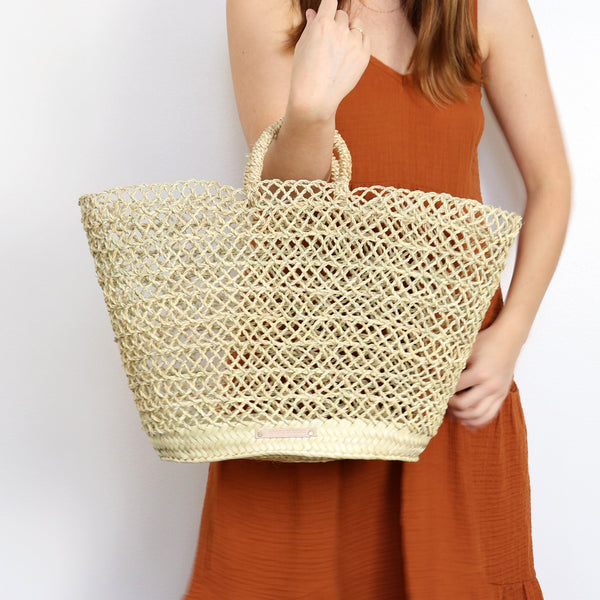 woman holding open weave handwoven straw market basket
