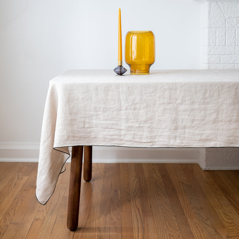 Natural beige linen tablecloth with black edge on dining table