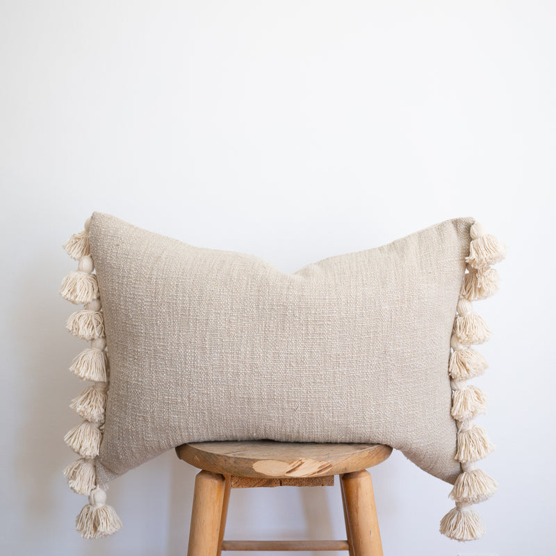 natural and neutral toned beige/sage woven rectangular pillow with fat tassels on edges